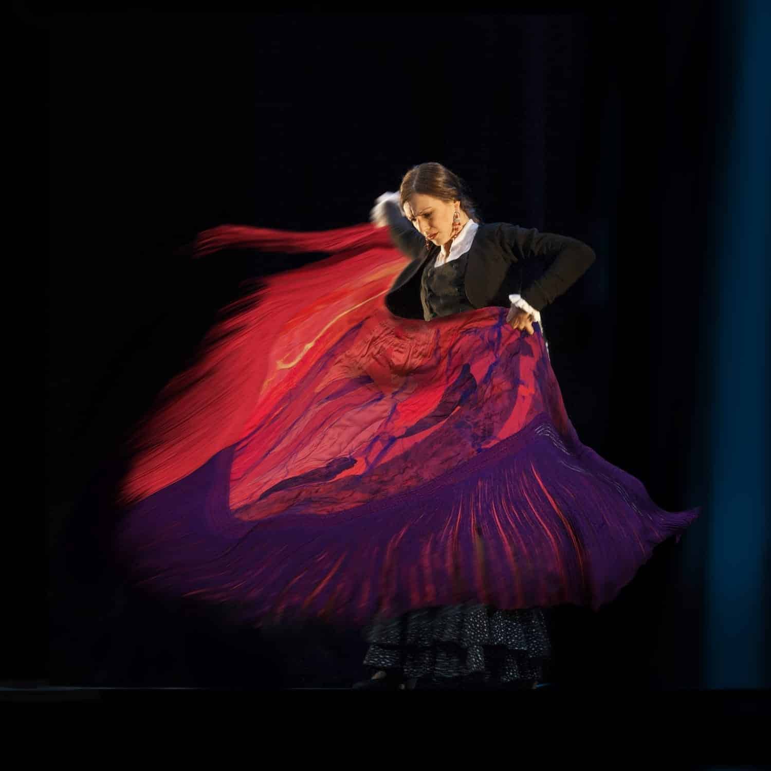 Mónica Vázquez bailando en un escenario con un mantón rojo y morado en pleno giro