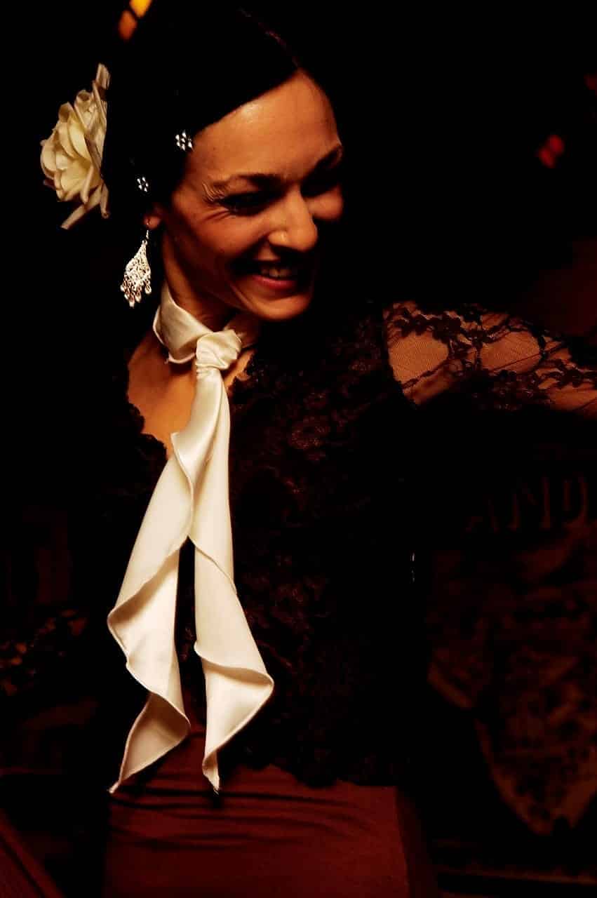 Bailaora de flamenco sonriendo, con una flor en el pelo y blusa de encaje negra con chorrera blanca