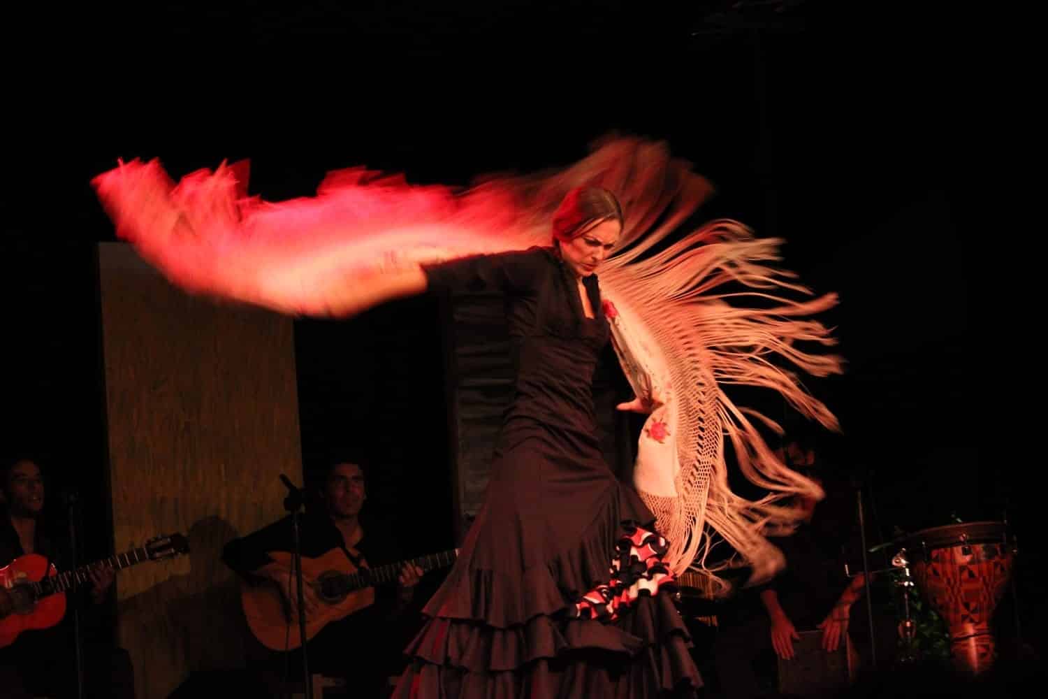 Mónica Vázquez bailando en un tablao con un mantón de flecos, con guitarristas al fondo