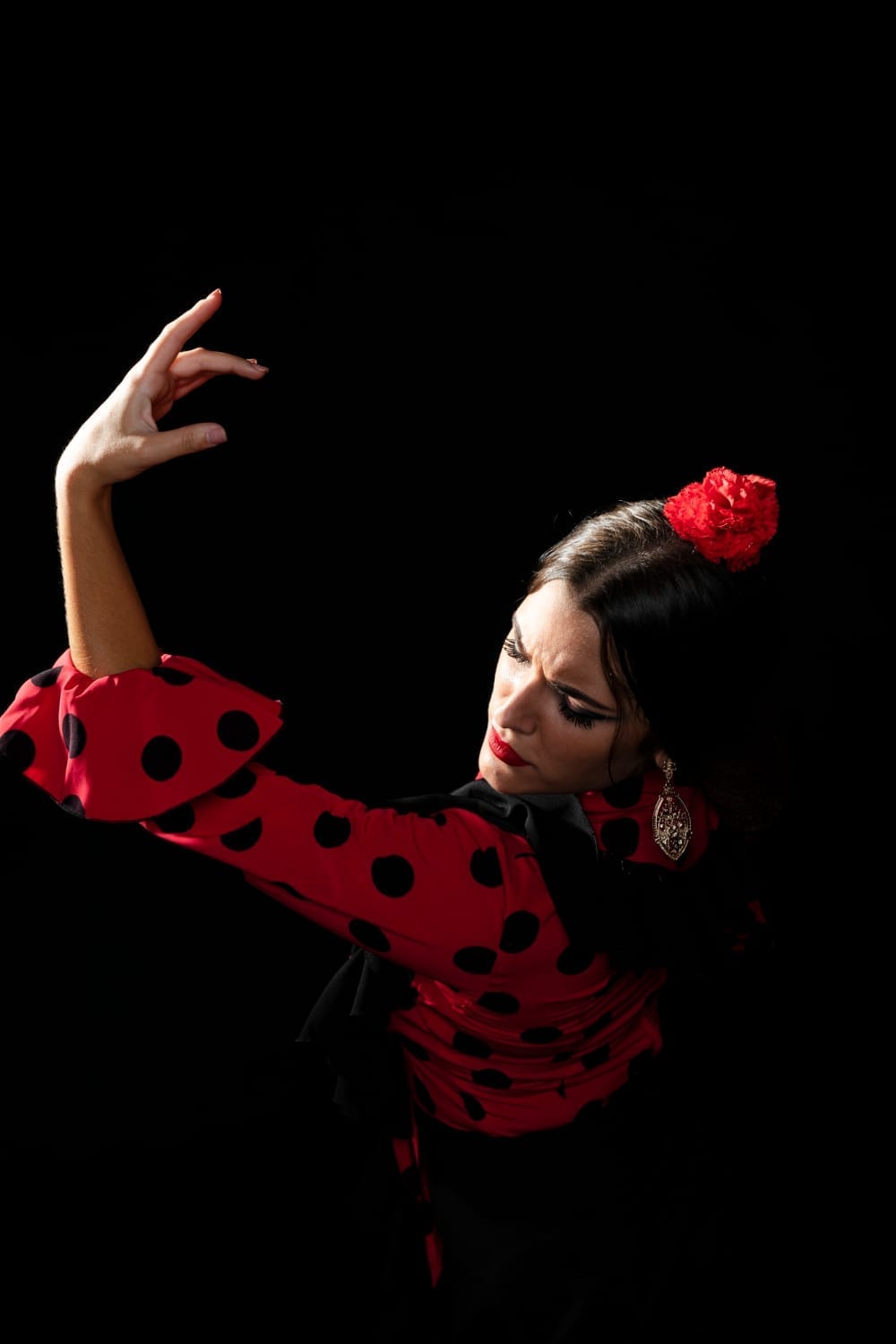 Bailaora de flamenco con vestido rojo de lunares y una flor roja en el pelo, con un brazo en alto