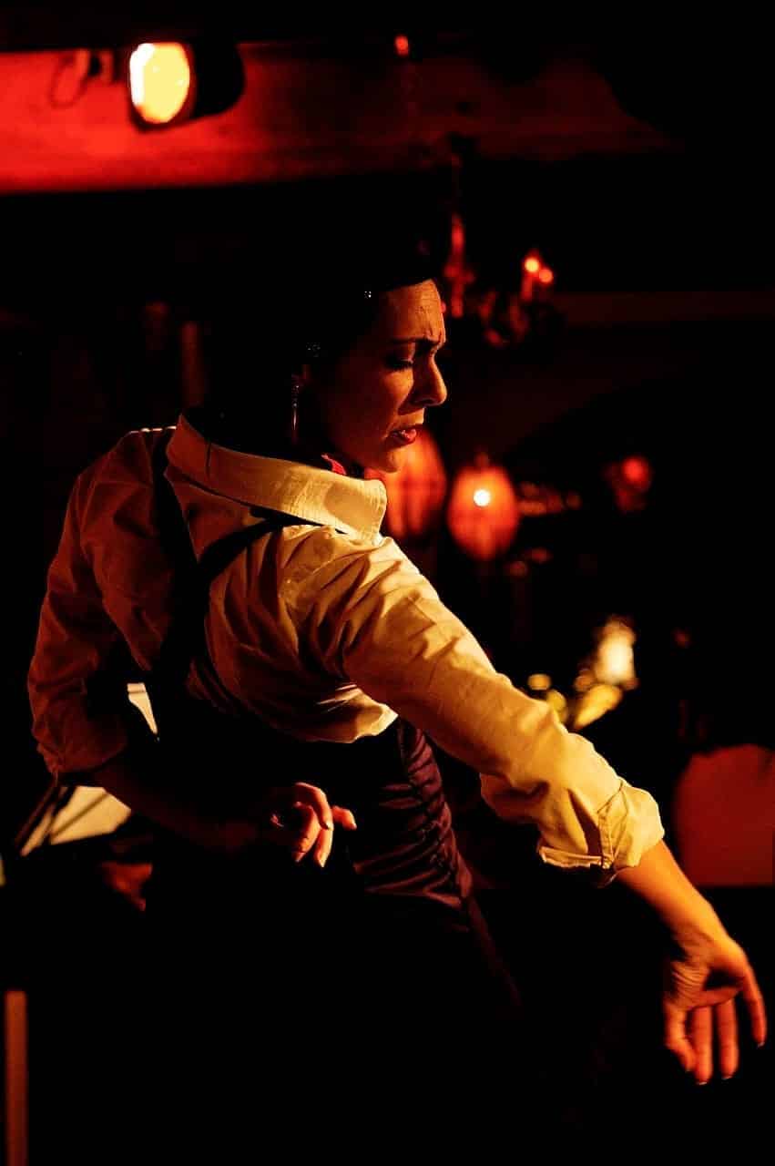 Persona bailando flamenco en un tablao iluminado en rojo, con camisa clara y chaleco
