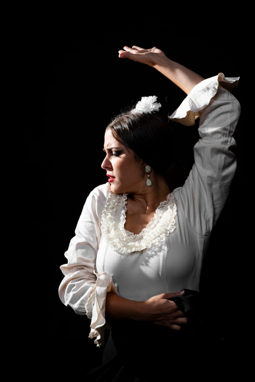 Bailaora de flamenco con blusa blanca de volantes y una flor blanca en el pelo, con el brazo levantado