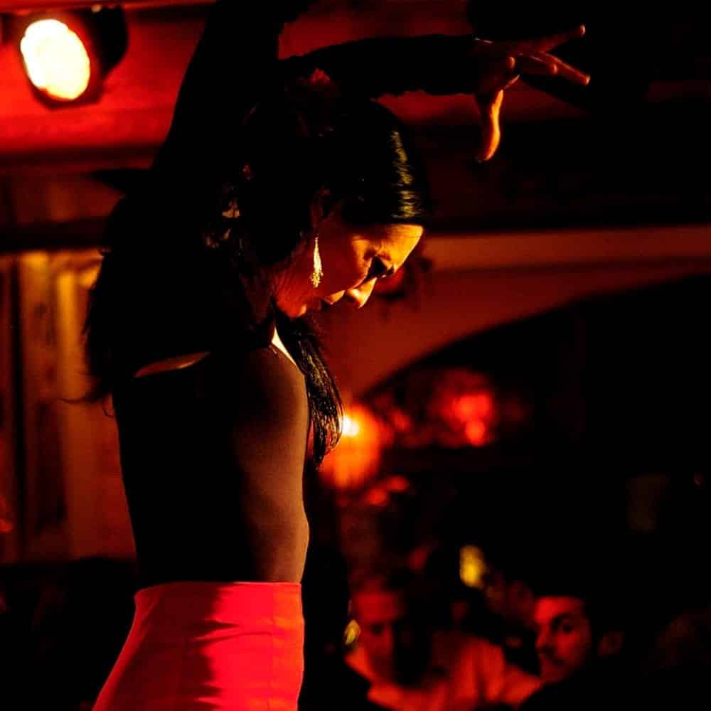 Bailaora de flamenco con los brazos en alto y falda roja en un tablao con luces rojas