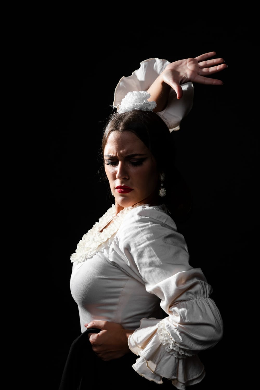 Bailaora de flamenco de perfil con blusa blanca de volantes y la mano en alto