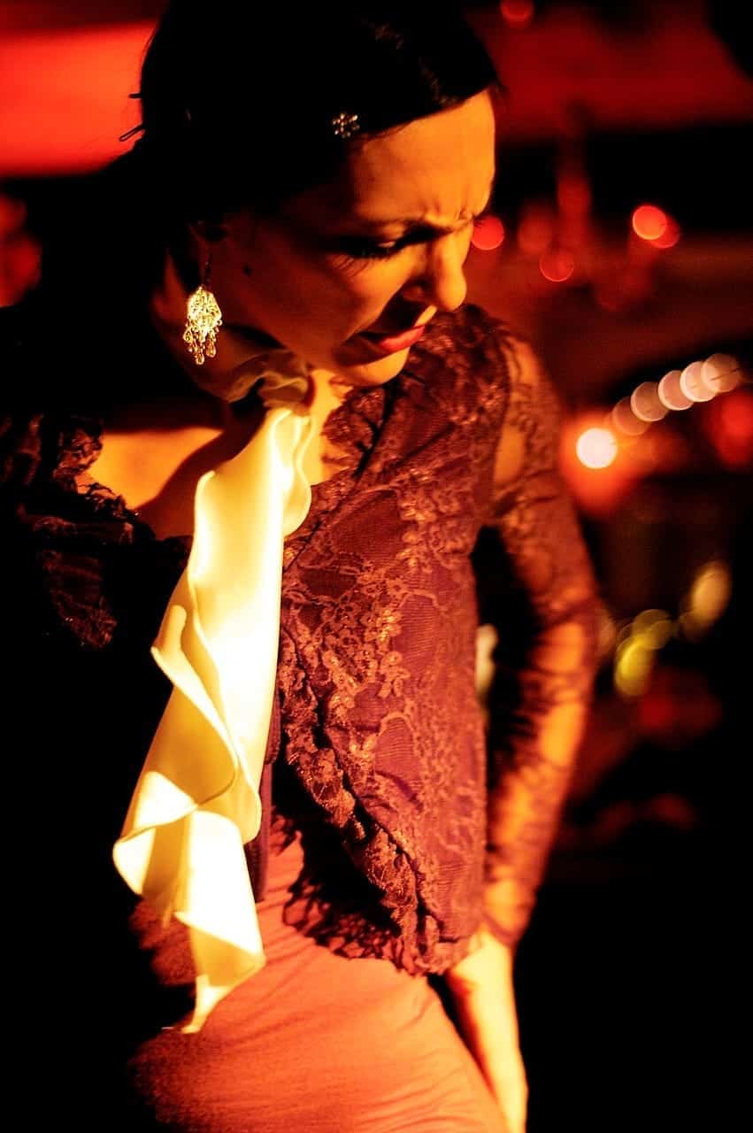 Bailaora de flamenco en un tablao, con la cabeza inclinada, blusa de encaje y chorrera clara