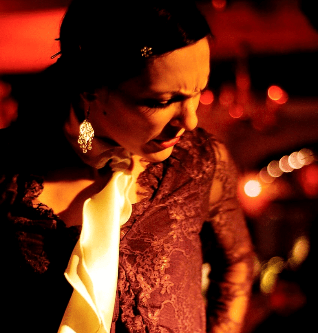 Primer plano de una bailaora de flamenco con blusa de encaje, chorrera clara y pendientes