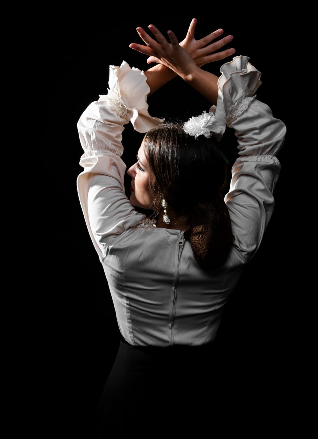 Bailaora de flamenco de espaldas con blusa blanca de volantes y las manos cruzadas sobre la cabeza