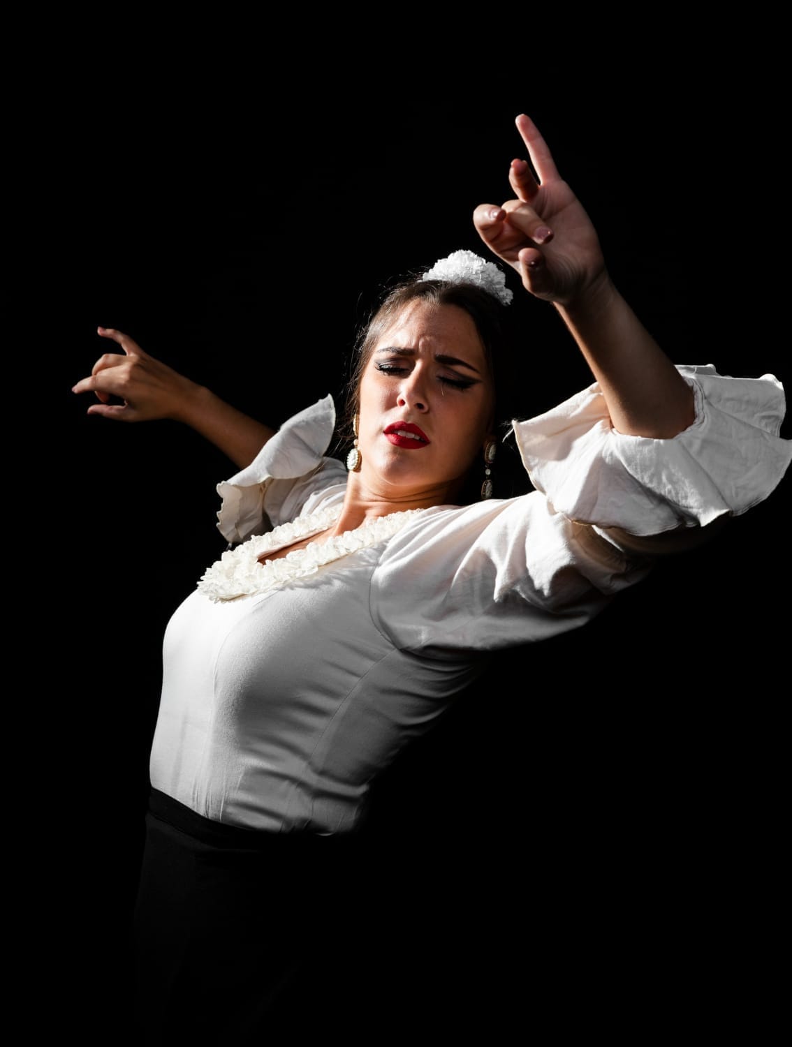 Bailaora de flamenco con blusa blanca de volantes, un brazo en alto y gesto concentrado