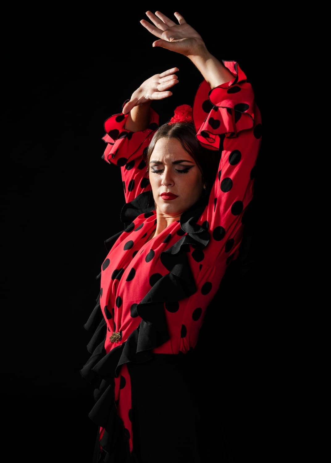Bailaora de flamenco con traje rojo de lunares y volantes negros, con los brazos en alto